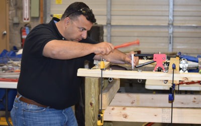 A man works on a woodworking project, using clamps and tools to secure wooden beams in a workshop setting. This demonstrates hands-on construction skills.